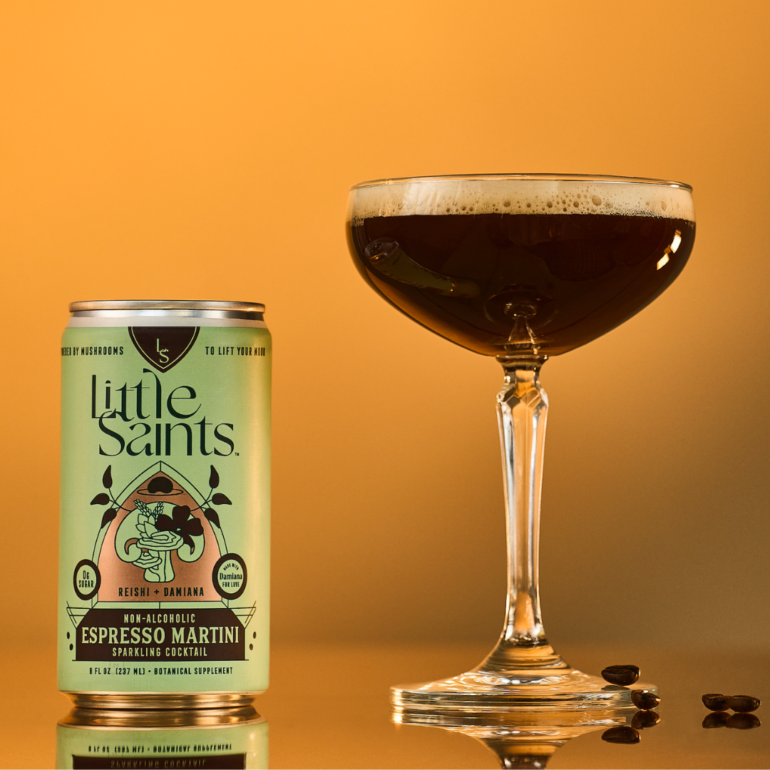 A can of Little Saints Espresso Martini Adaptogenic Mocktail sits beside a filled martini glass on a gold surface with three coffee beans, set against a warm golden orange gradient background.