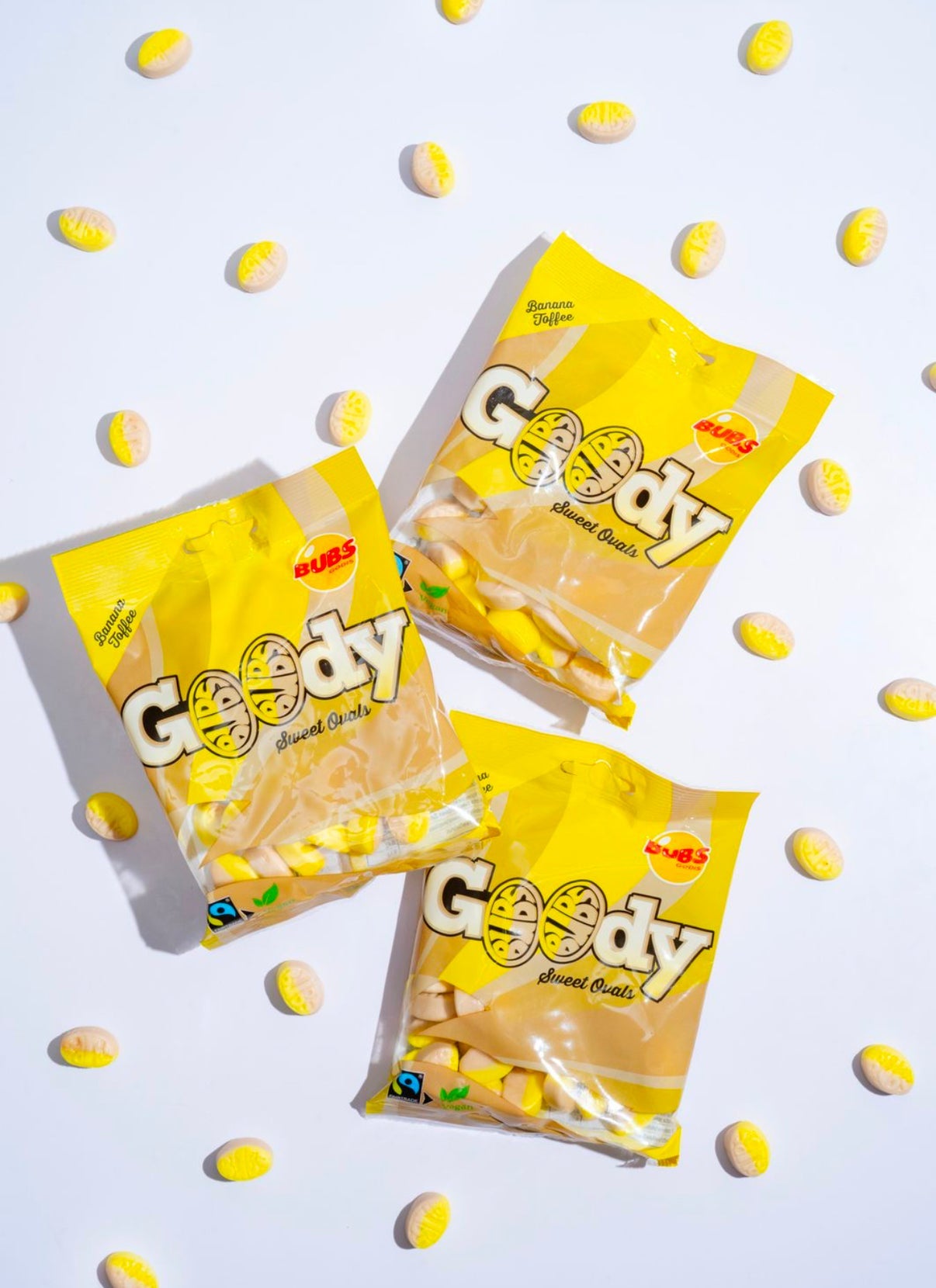 Banana Toffee Swedish Candy Gummies in yellow Goody bags with individual yellow and white oval gummies on white background.