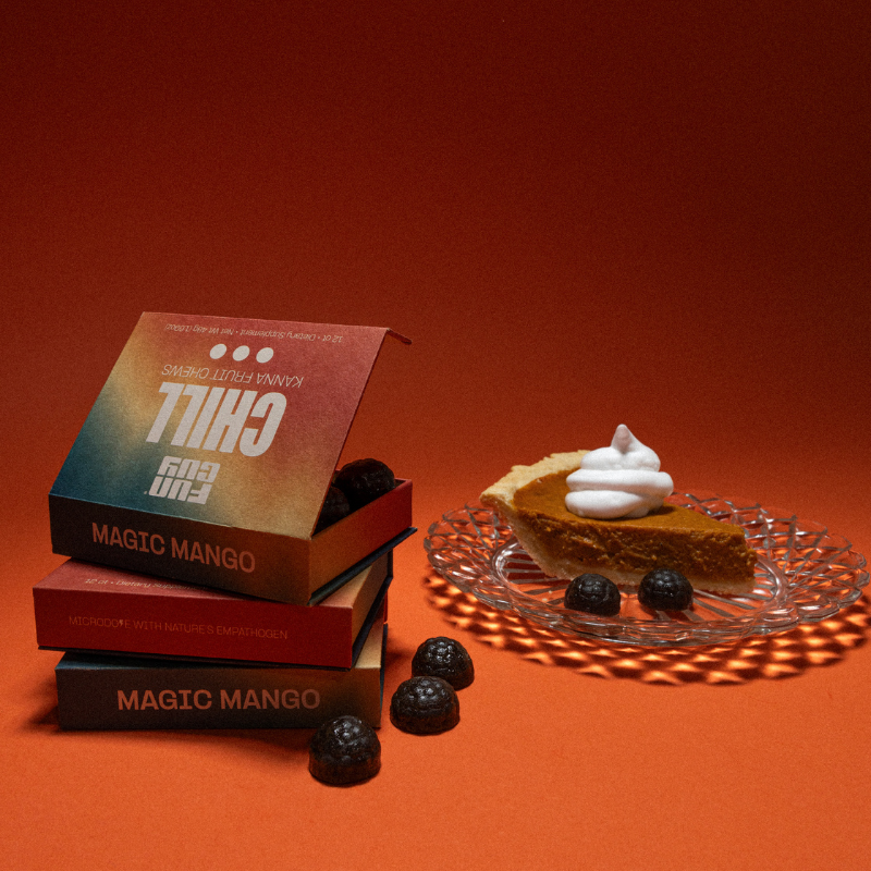 Three boxes of Fun Guy Chill Fruit Chews stacked on an orange surface beside chocolate candies and a slice of pie with whipped cream, all set against an orange background—the perfect treat for stress relief.