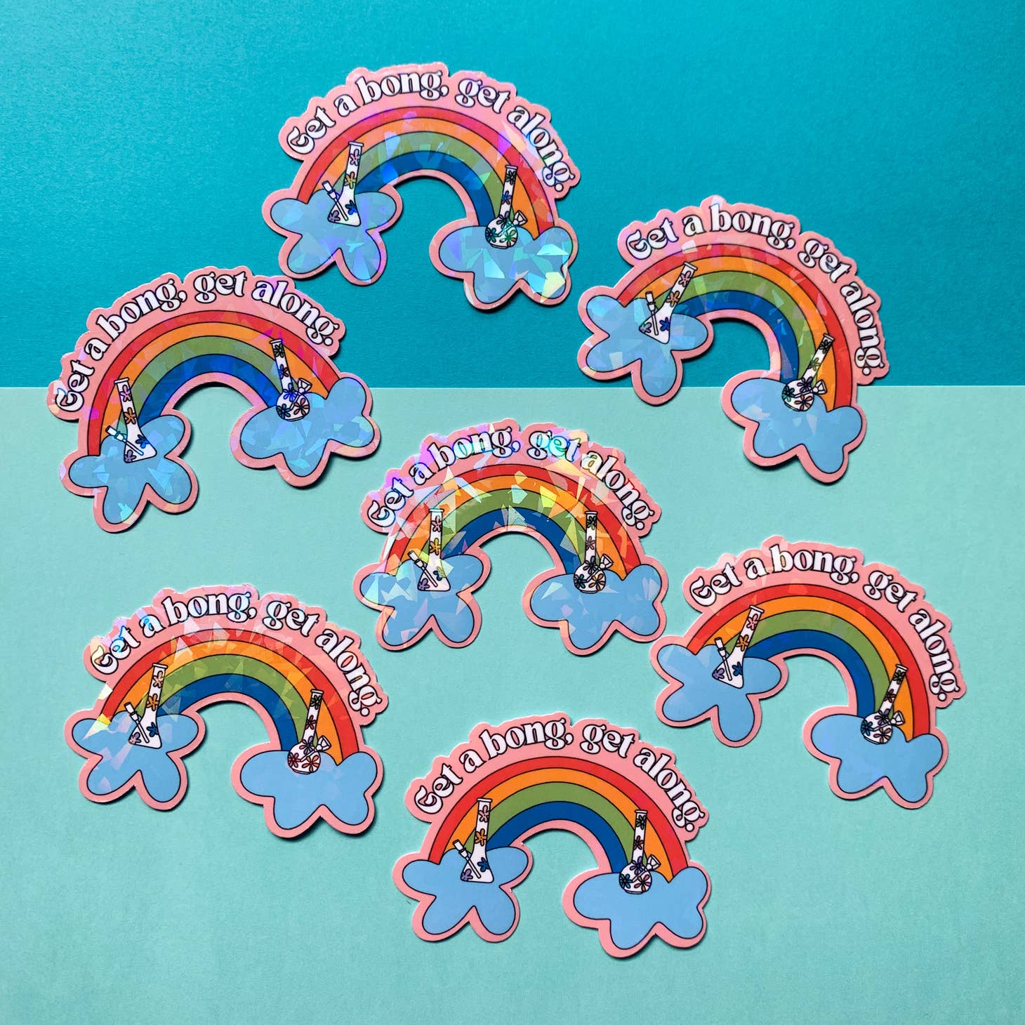 The Get-A-Bong Sticker by Han Made features vibrant rainbows ending in blue clouds, each with a hand holding a bong and the phrase “Get a bong, get along!” Printed on waterproof vinyl over a teal and aqua background.