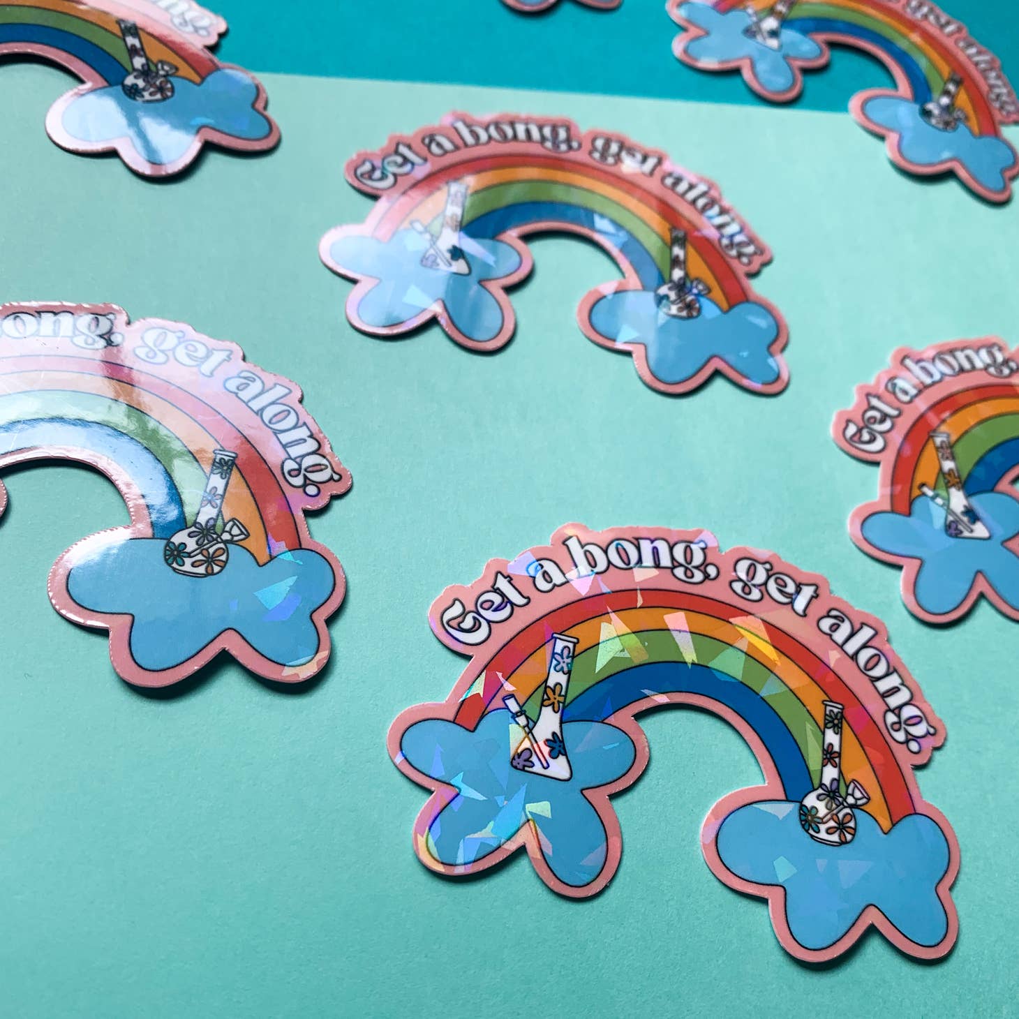 The Han Made Get-A-Bong Sticker features a rainbow, clouds, and a bong with “Get a bong, get along!” on waterproof vinyl. Its playful design pops against mint green, making it a fun addition to any collection.