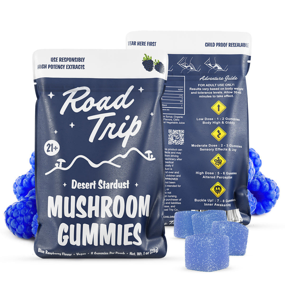 Two blue pouches of Road Trip Mushroom Gummies by Road Trip are shown, with blue raspberry plant-based gummies in front and behind. The packaging displays dosage details and a mountain design.