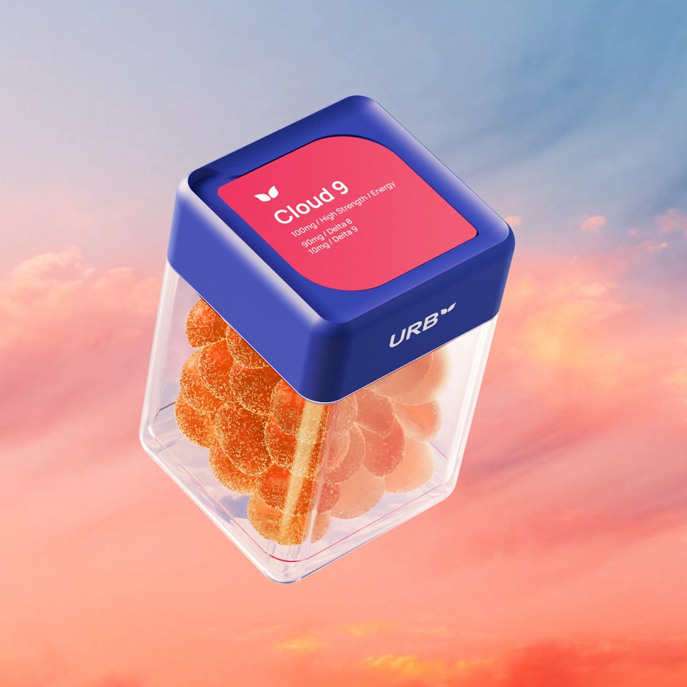 A clear plastic jar of Sky Bites THC Gummies by URB, filled with orange gummies and topped with a blue lid, floats against a dreamy sky of pink and orange clouds. The label highlights “Lemon/Lime/Energy.”.
