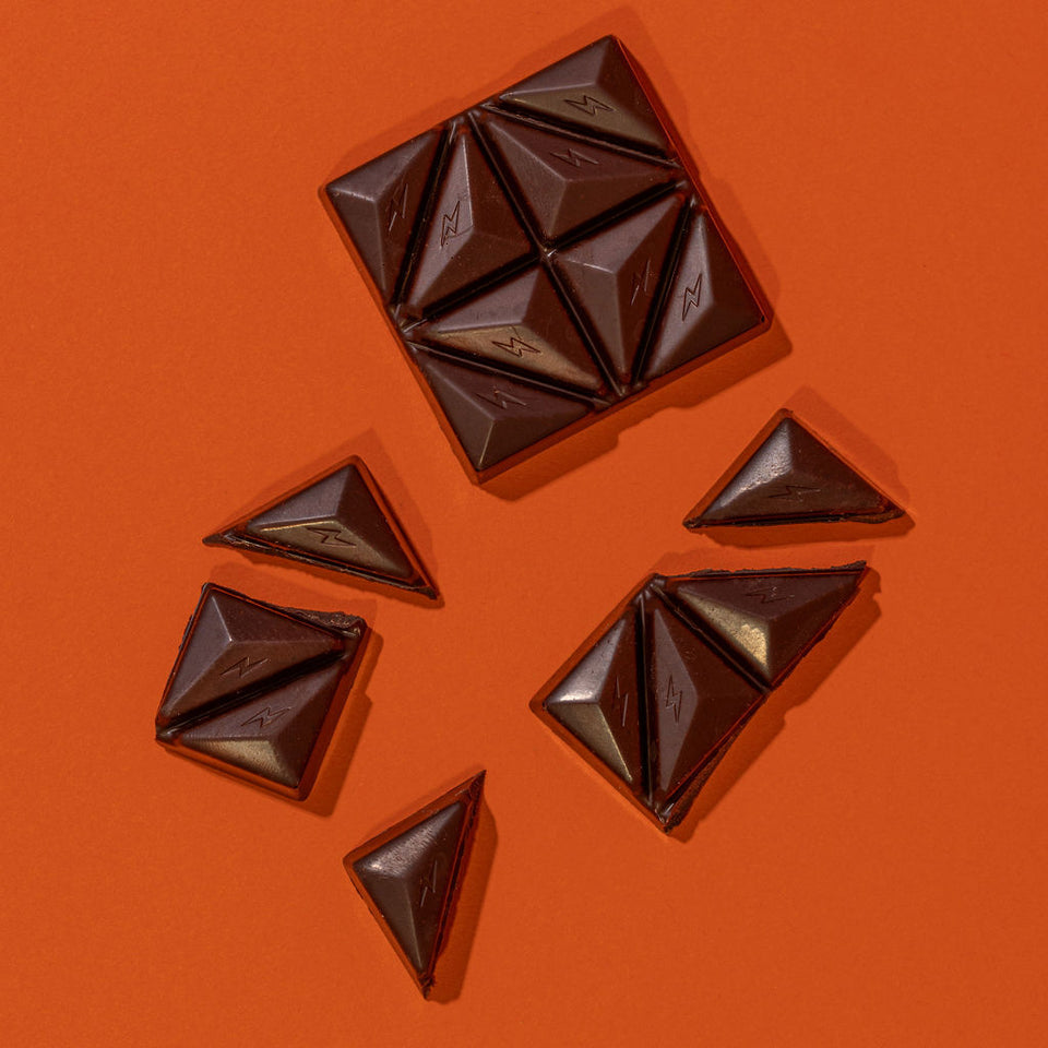 Fun Guy’s Chill Chocolate bar, featuring triangular pieces—some set apart from the main square—sits on an orange backdrop, making it a perfect pick-me-up for any chocolate lover.