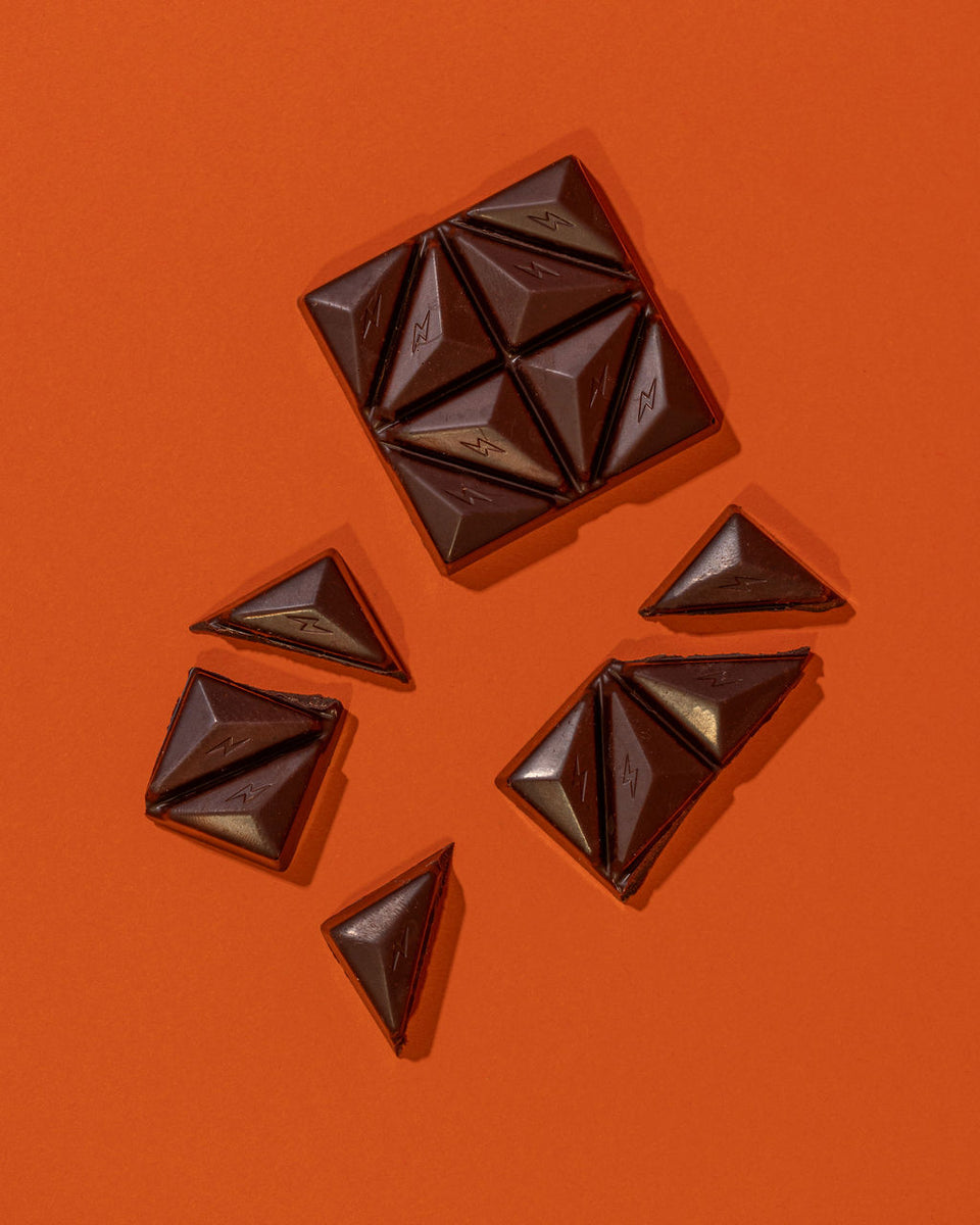 Fun Guy’s Chill Chocolate bar, featuring triangular pieces—some set apart from the main square—sits on an orange backdrop, making it a perfect pick-me-up for any chocolate lover.