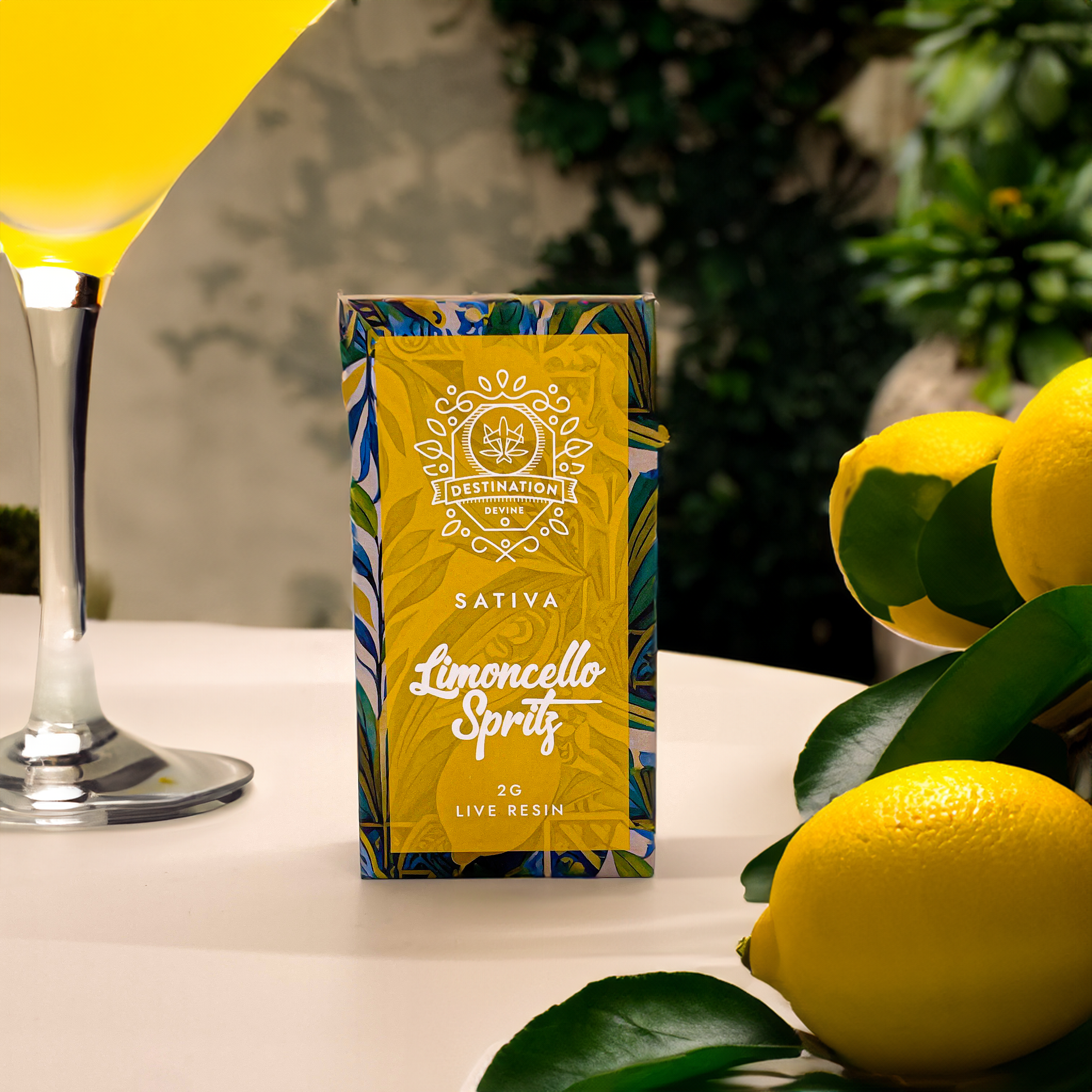 A box labeled deVINE Destinations Live Resin THC Disposable by DeVINE Wellness sits beside fresh lemons, leafy greens, and a yellow drink—perfect for adventure-ready vaping—all set against a softly blurred natural backdrop.