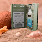 A DeVINE Wellness Destinations Live Resin THC Disposable vape is showcased in an open box on a sandy beach with seashells, a starfish, and coconut, highlighting the Polynesian Mai Tai hybrid strain and travel-inspired design.