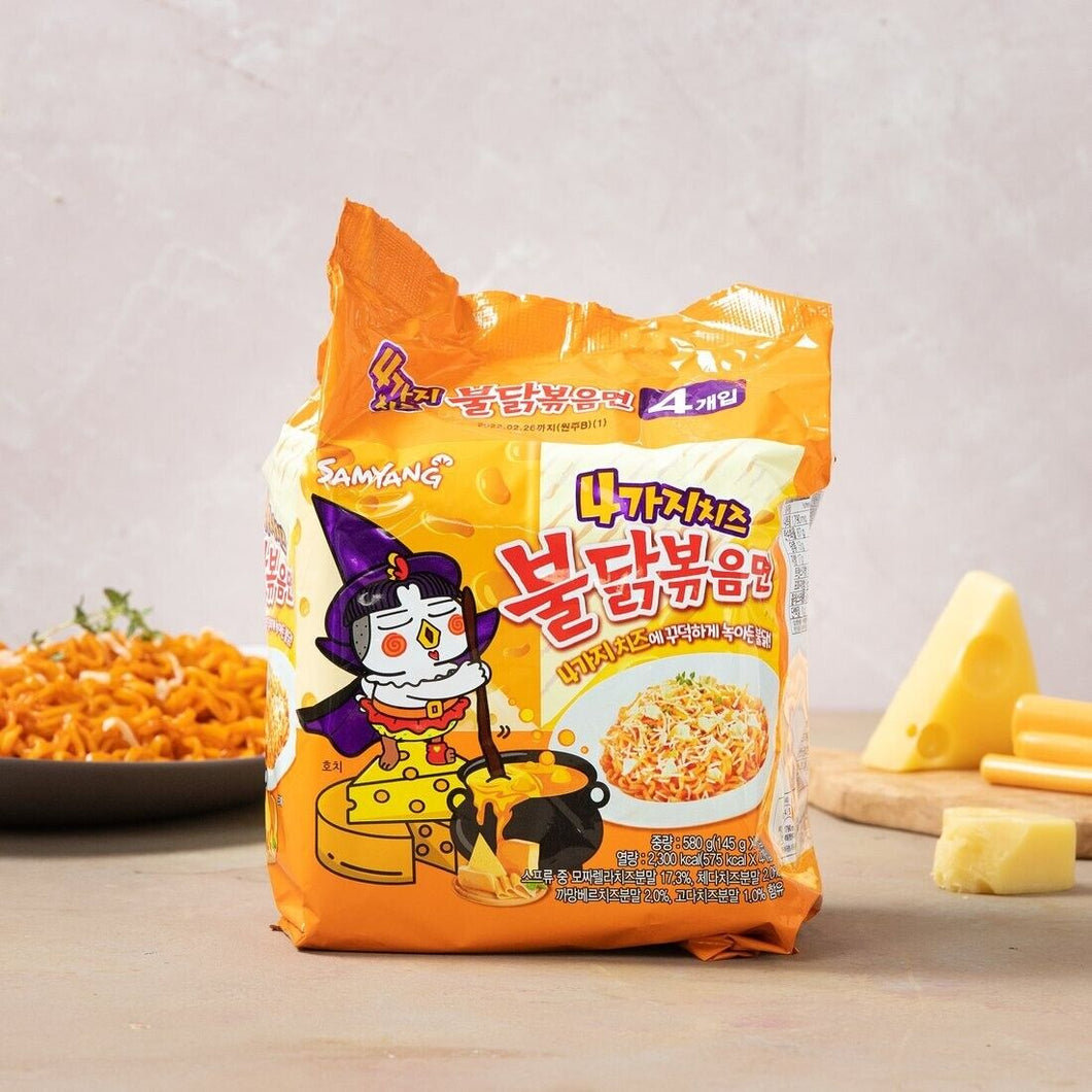 A pack of Exotic Snacks Buldak Spicy Chicken Quattro Cheese Ramen sits on a table with its cartoon chicken mascot, alongside a plate of cooked spicy noodles and pieces of cheese on a wooden board.