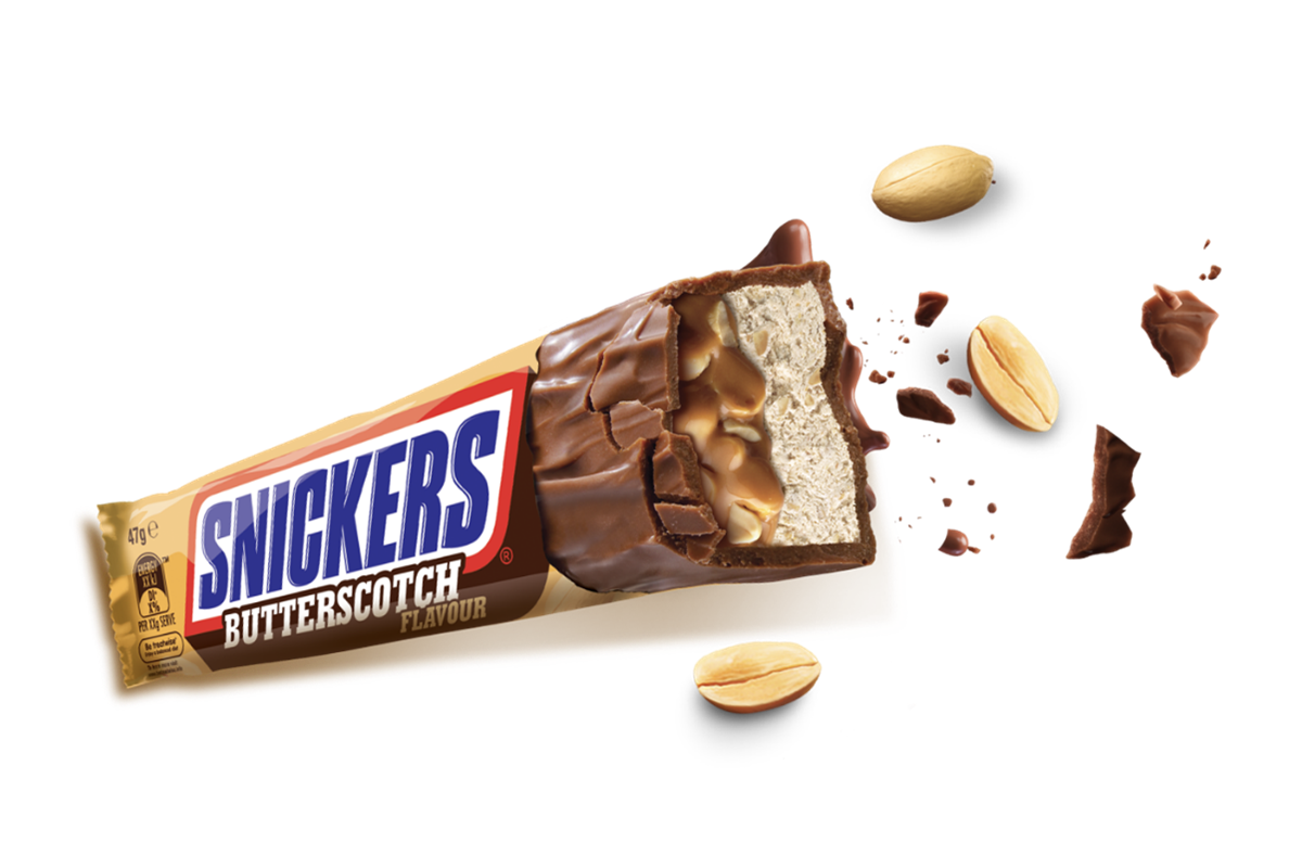A Snickers-Butterscotch bar by Exotic Snacks with a bite taken out reveals caramel and nougat inside butterscotch chocolate, surrounded by whole and broken peanuts on a white background.
