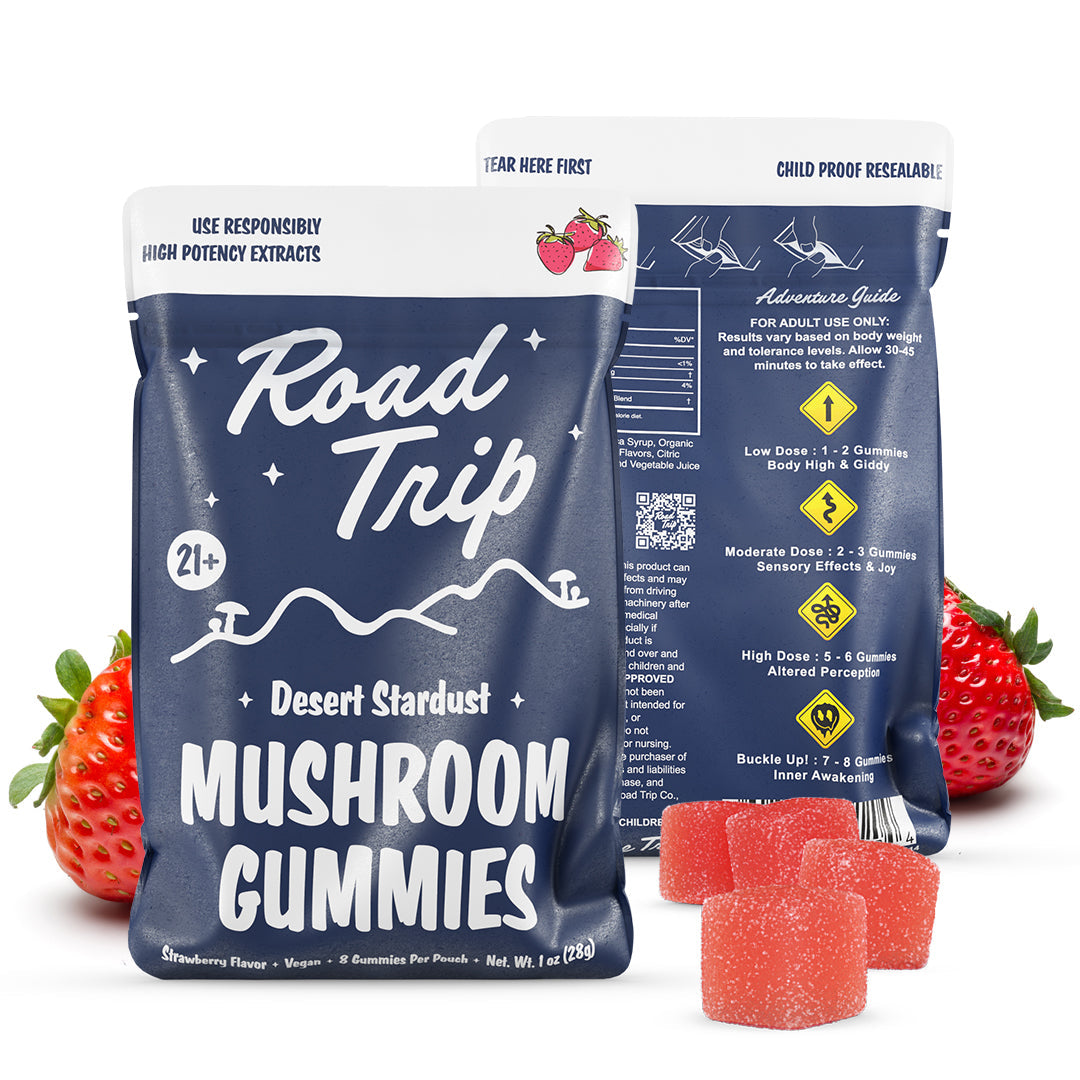 Two blue and white Road Trip Mushroom Gummies bags are shown, featuring vegan strawberry-flavored pink gummies in front. The back of the packaging displays a dosage guide and safety information.