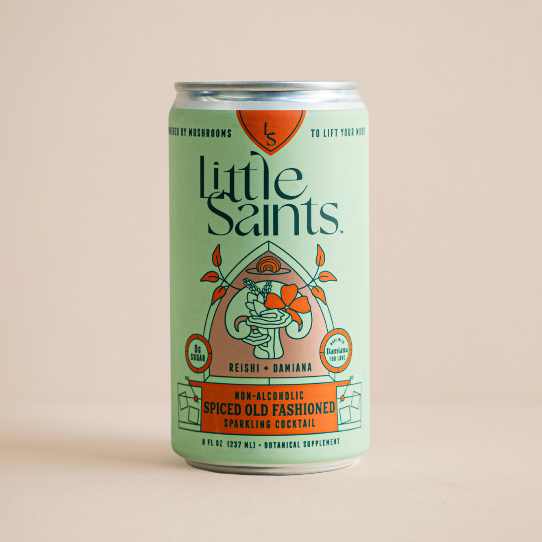 A green can of Little Saints Spiced Old Fashioned Adaptogenic Mocktail displays botanical designs, orange highlights, and a label noting non-alcoholic spirits with reishi mushroom and Infused with mushrooms clearly featured.