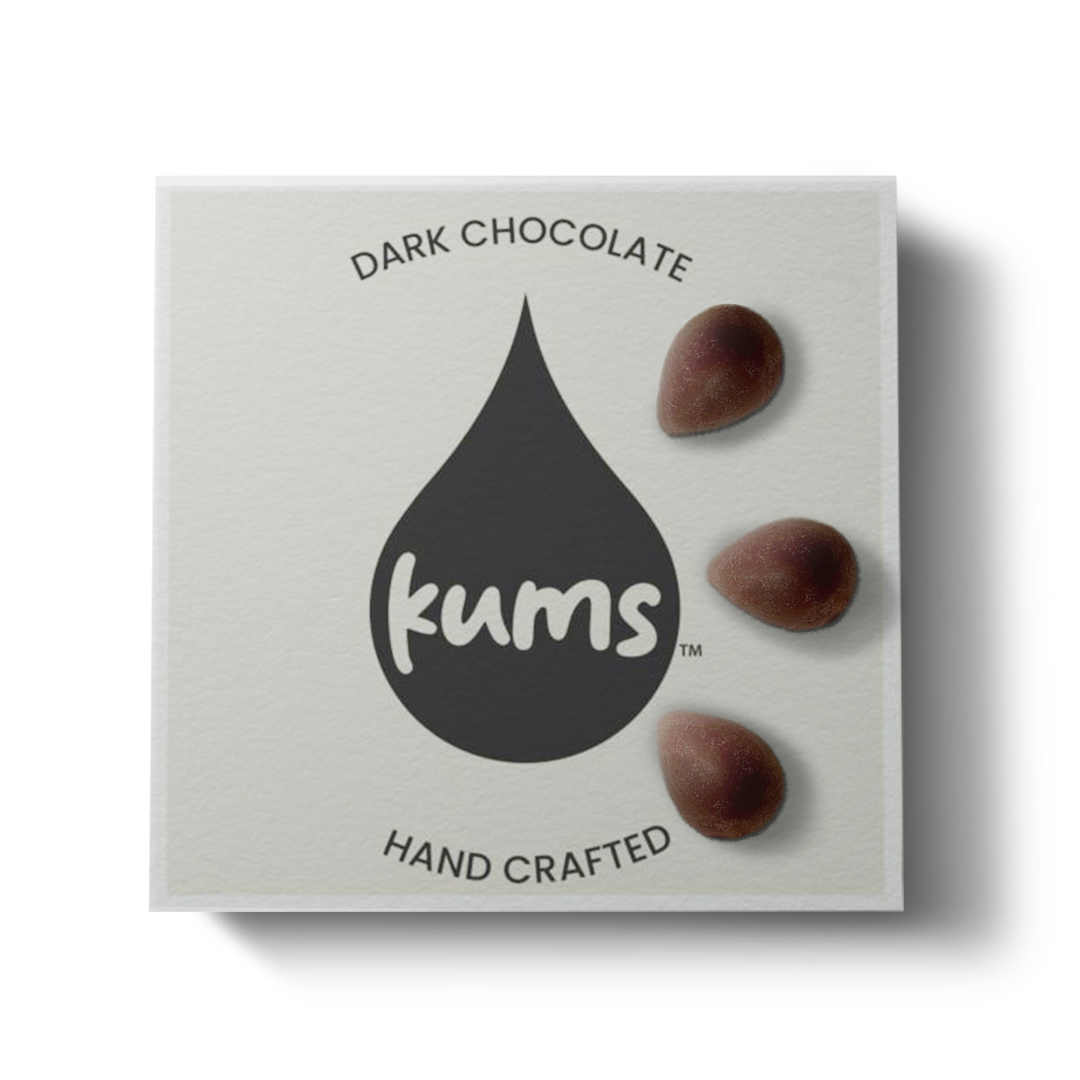 A square box labeled Kums Chocolate for Couples features a large black drop, DARK CHOCOLATE above, HAND CRAFTED below, and three chocolates on the right hinting at couples intimacy and indulgence. Brand: Kums.