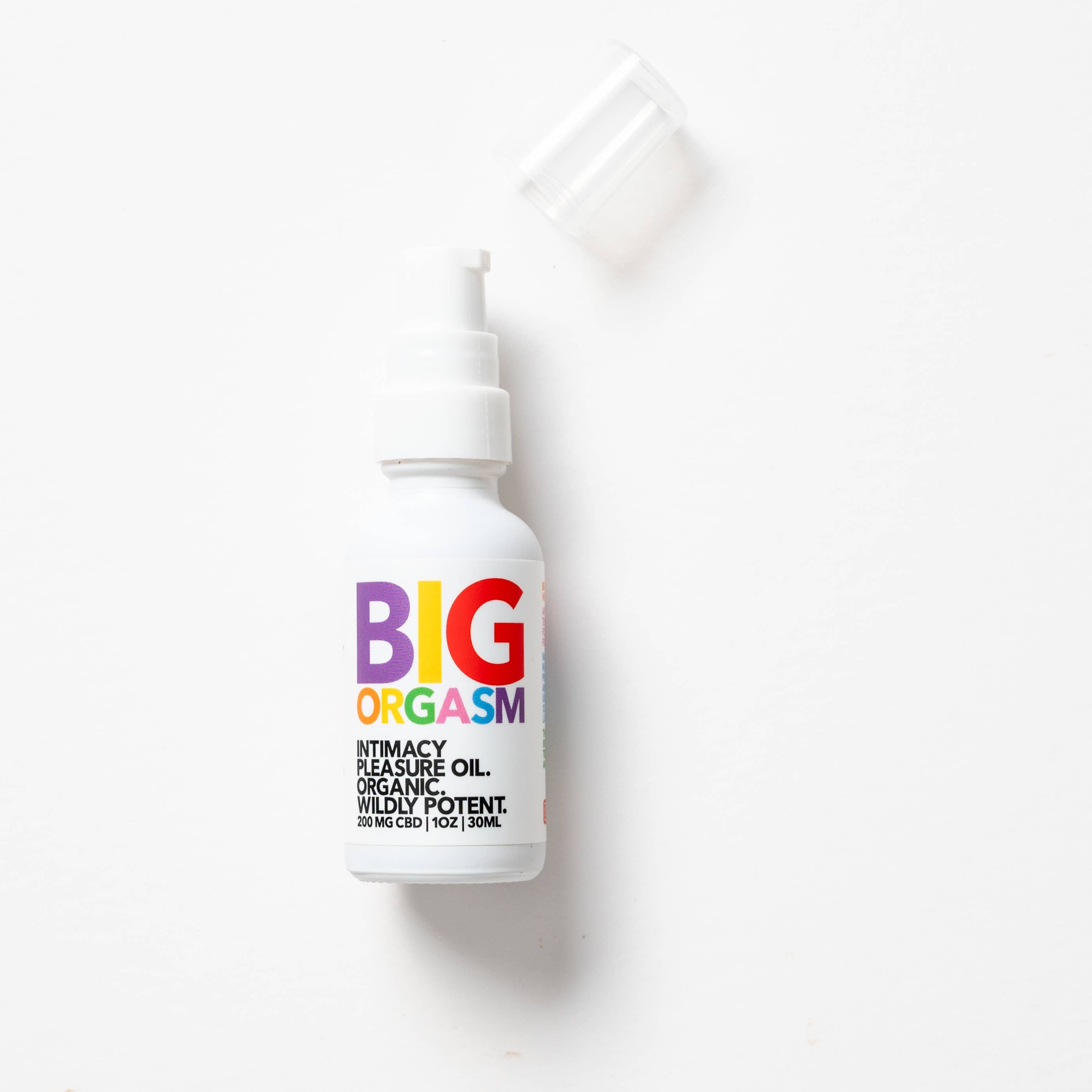 A white bottle of Eat Gold Organics Big Orgasm Oil, labeled in colorful text, rests on a white surface with its clear cap nearby. This organic arousal oil with damiana leaf is made to enhance intimacy and pleasure.
