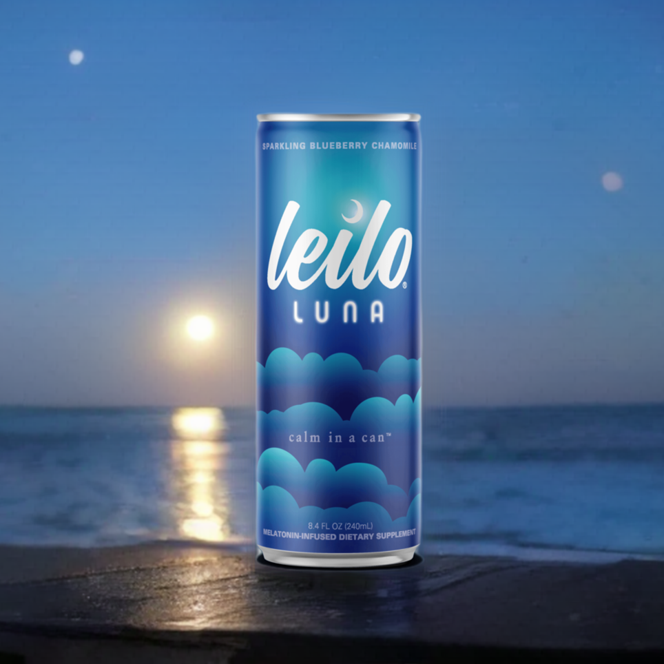 A can of Leilo Luna by Leilo, a sparkling blueberry chamomile sleep drink with kava and melatonin, sits by the ocean at night beneath a full moon and stars. The label reads “calm in a can.”.