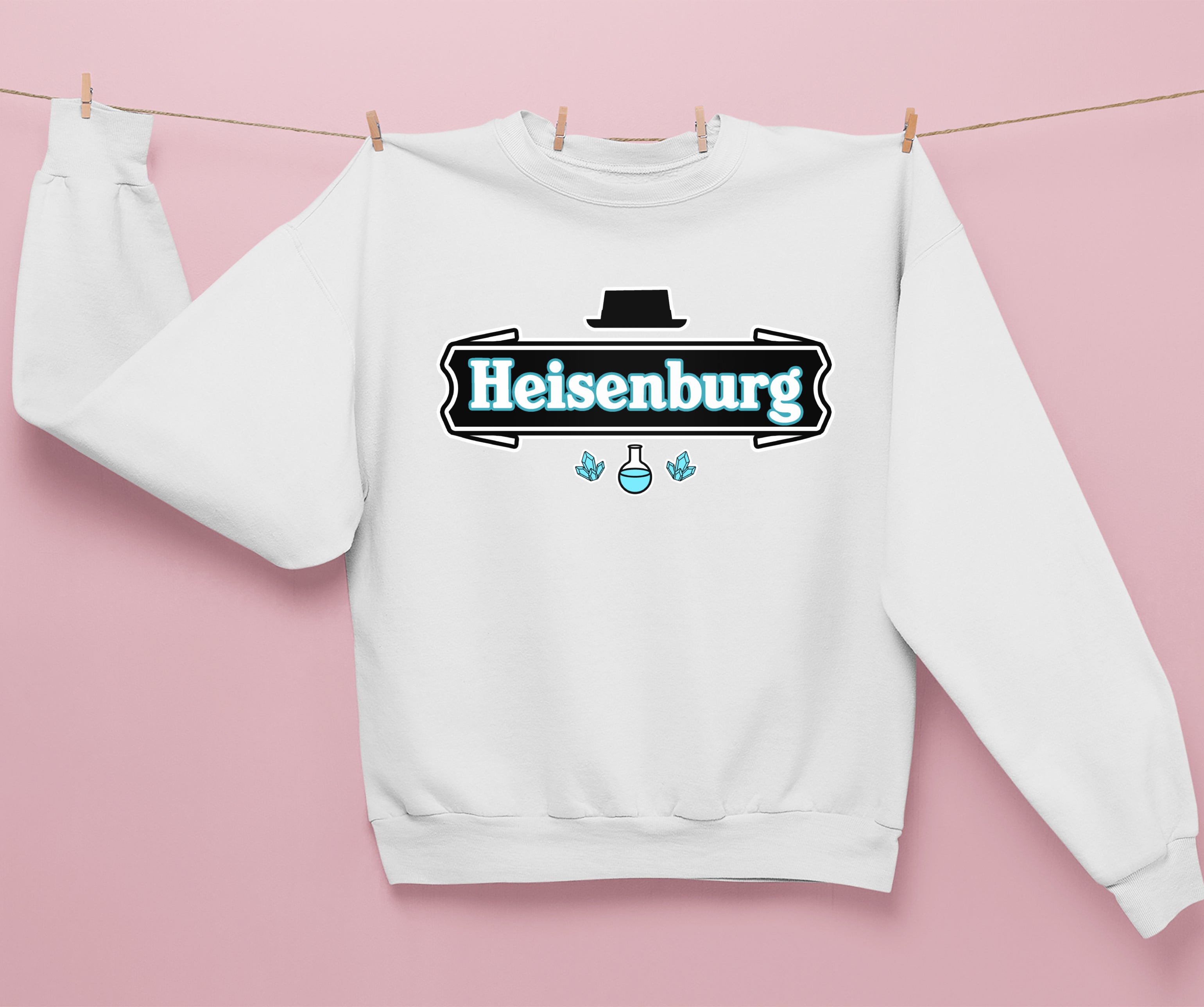 The HiCiti Heisenberg Crewneck Sweatshirt, in white, hangs on a clothesline against a pink background and features a graphic with Heisenberg, a black hat, beaker, and two blue crystals.