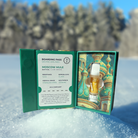 A green DeVINE Destinations Live Resin THC Cartridge box by DeVINE Wellness sits open on snow, revealing a vape cartridge and St. Basil’s Cathedral art—ideal for travel-inspired vaping with Moscow Mule live resin details amid snowy trees.