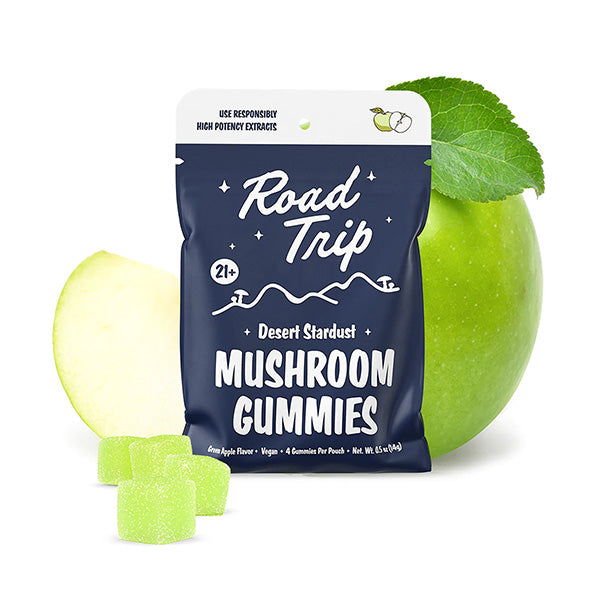 A blue Road Trip Mushroom Gummies pouch stands in front of a green apple and leaf, with three green plant-based gummies displayed beside it.