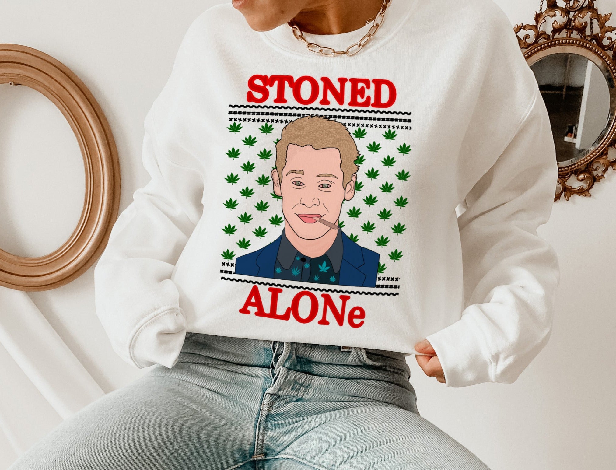 A person wears the HiCiti Stoned Alone Crewneck Sweatshirt, a unisex cotton top featuring a cartoon man with a cigarette, marijuana leaves, and STONED ALONe in bold red letters above and below the design.