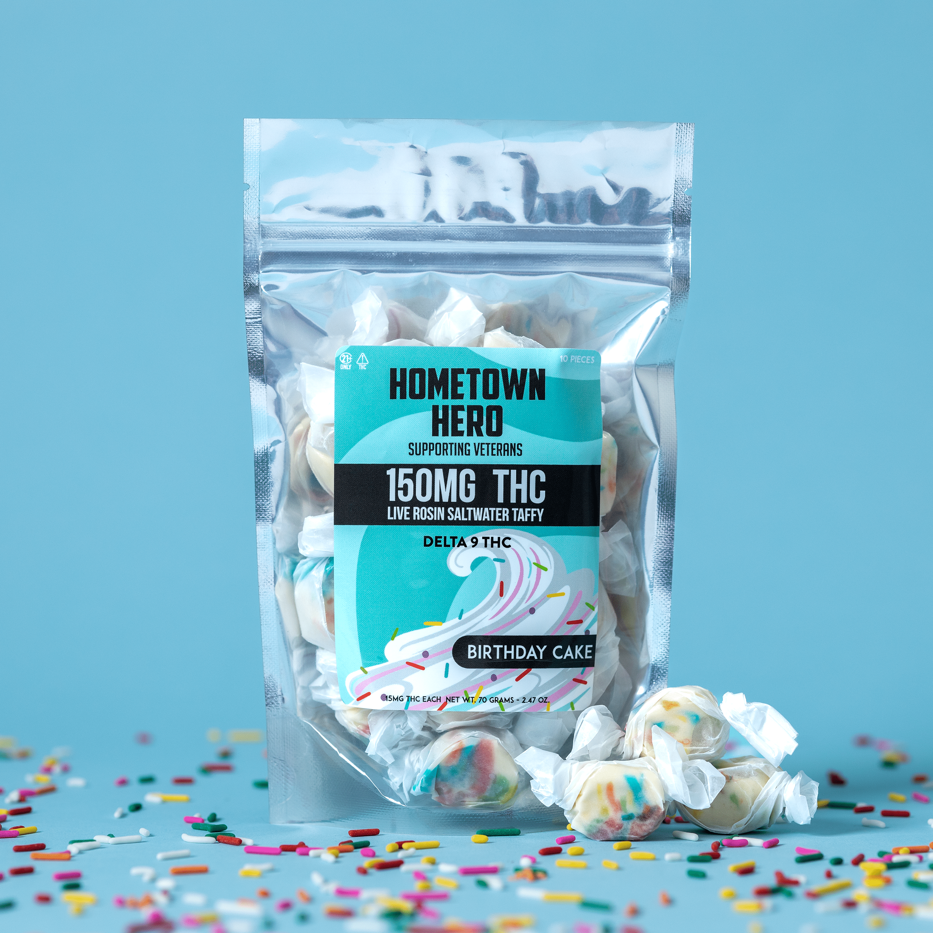 A clear resealable Hometown Hero Delta-9 Live Rosin Taffy bag stands on a blue surface, surrounded by individually wrapped live rosin infused candies and colorful confetti.