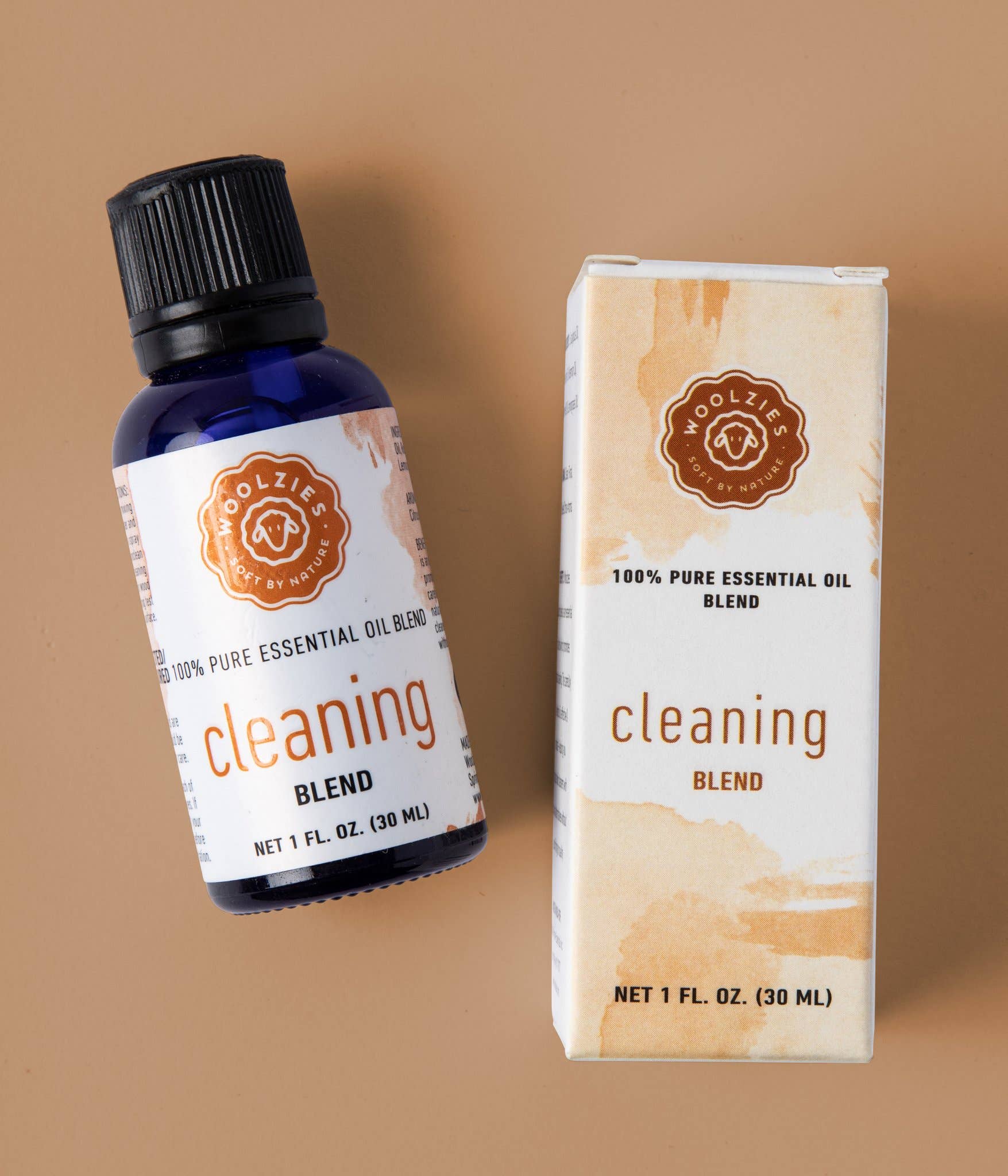 A blue bottle of Woolzies Cleaning Blend Essential Oil, 1 fl. oz. (30 ml), is shown beside its white and orange box on a beige background—a natural cleaner for fresh, inviting spaces.