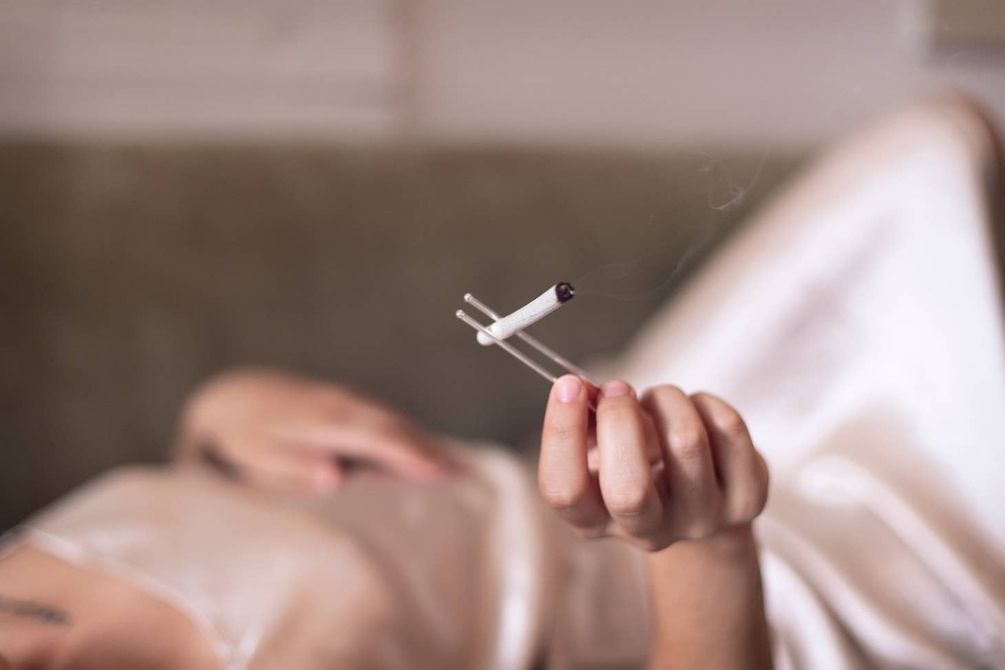 Wearing a silky, light dress, someone relaxes on a couch, elegantly holding the Frankie Smoke NECKLACE + CLIP SET as smoke drifts upward—adding sophistication to their smoking accessories.