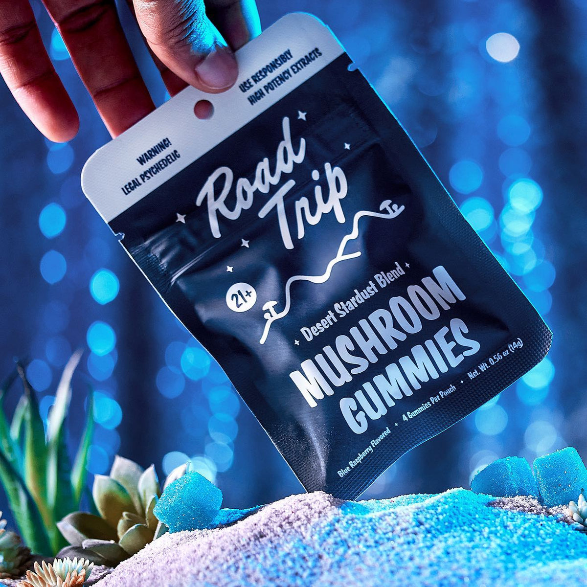 Hand holding a blue Road Trip Mushroom Gummies Desert Stardust blend pouch with a dreamy glow