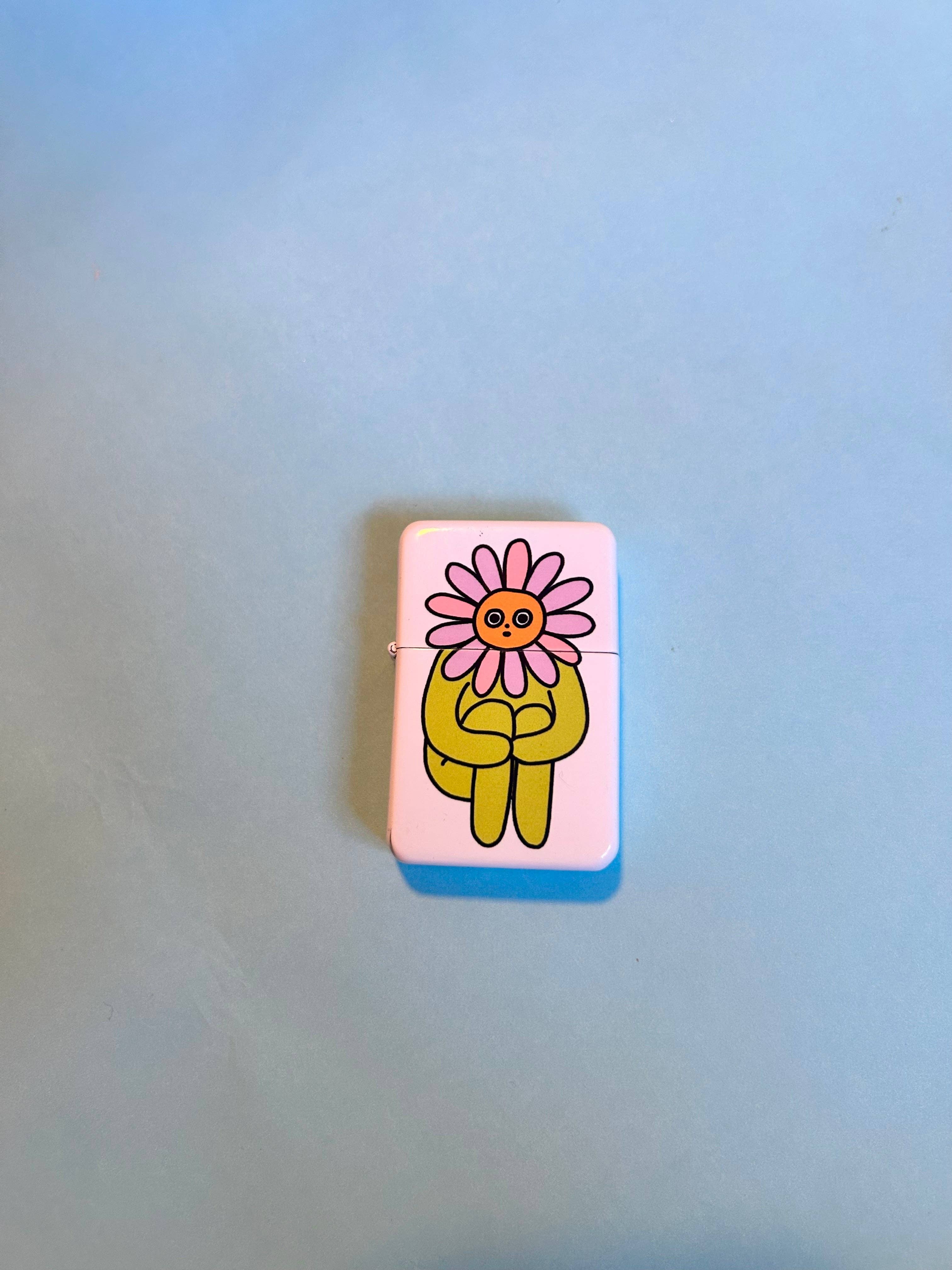 The Peach Fuzzs Flower Boy Lighter: Perfect features a cartoon yellow character with a pink flower head, sitting cross-legged on a light blue background—a quirky and fun gift for stoners.