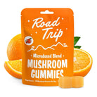 A pouch labeled Day Trip Microdosed Gummies by Road Trip stands before orange slices and two gummies. The package features white text, small mushroom and mountain illustrations, and highlights a microdose formula with Lion’s Mane mushroom.